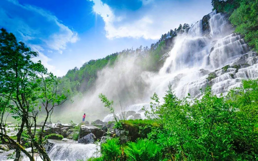 Tvindefossen waterfall cascading over rocks in Voss, Norway, surrounded by lush greenery.