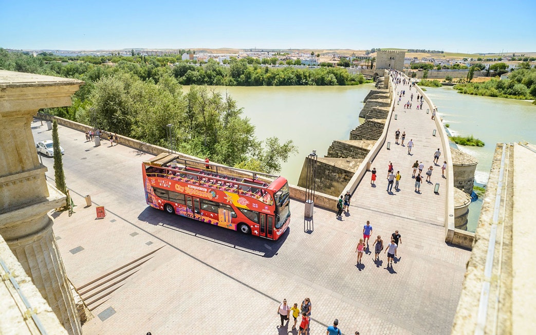 Open-top sightseeing bus near Roman Bridge in Cordoba, Spain.
