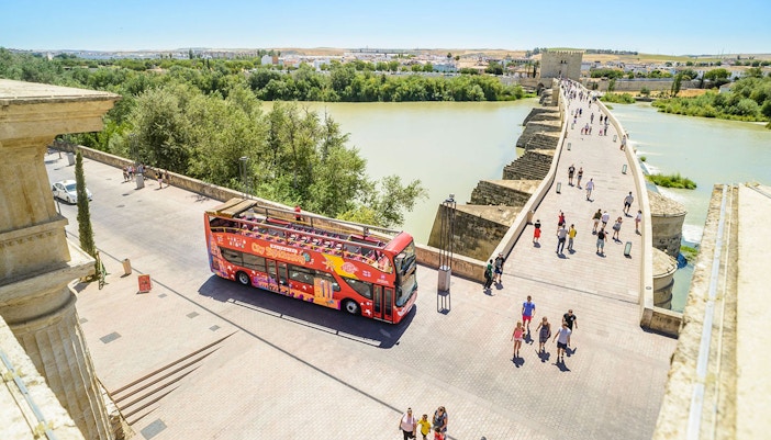 Open-top sightseeing bus near Roman Bridge in Cordoba, Spain.