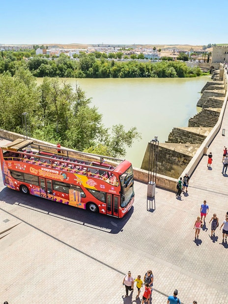 Open-top sightseeing bus near Roman Bridge in Cordoba, Spain.