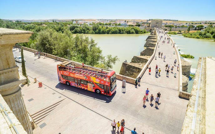 Open-top sightseeing bus near Roman Bridge in Cordoba, Spain.