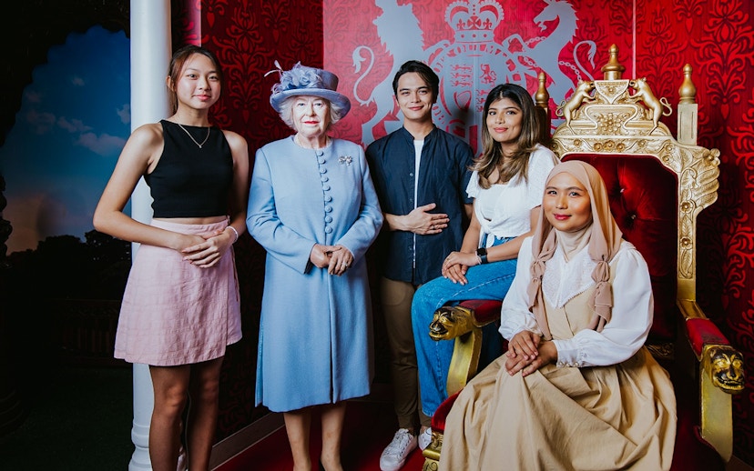 Visitors posing with a wax figure of the queen at Madame Tussauds Singapore.