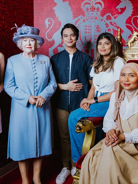 Visitors posing with a wax figure of the queen at Madame Tussauds Singapore.
