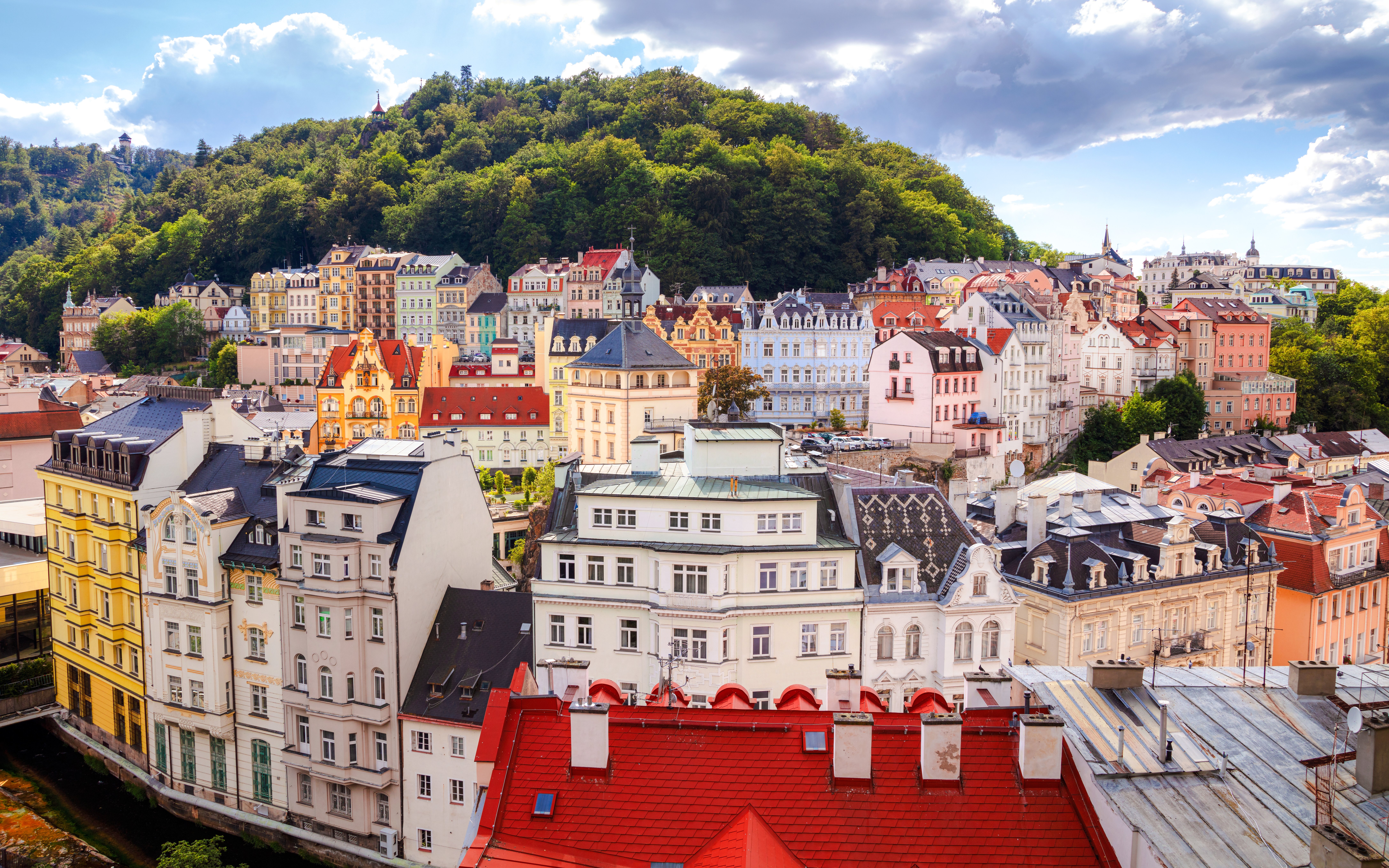 Colorful historic buildings in Karlovy Vary with lush green hills in the background.