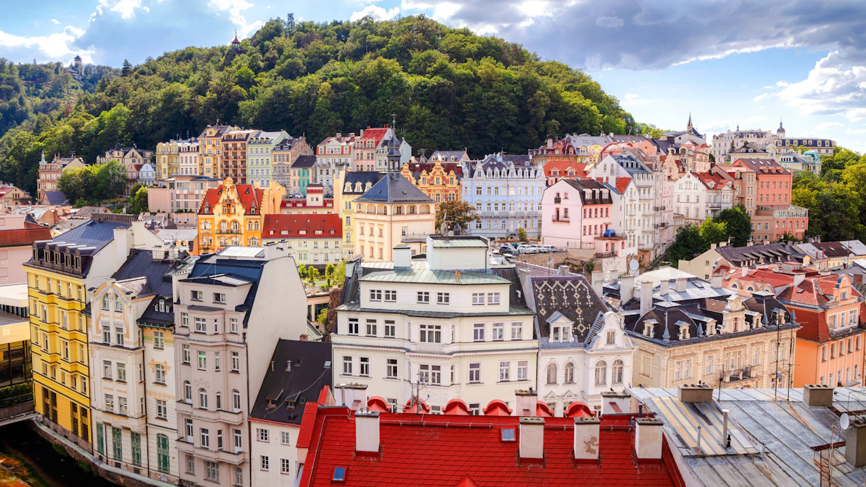Colorful historic buildings in Karlovy Vary with lush green hills in the background.