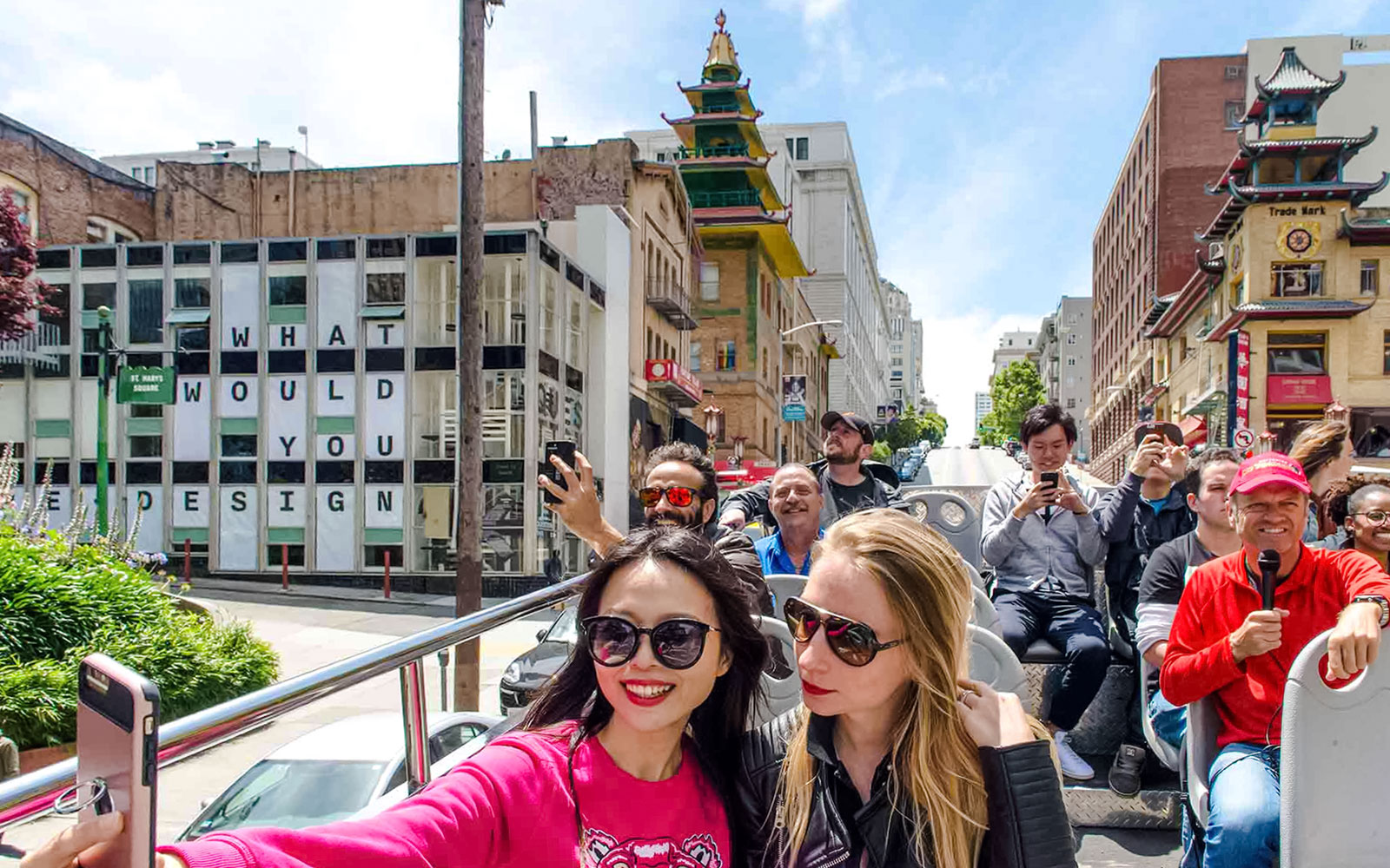 Open-top bus tour in San Francisco's Chinatown with tourists taking photos.
