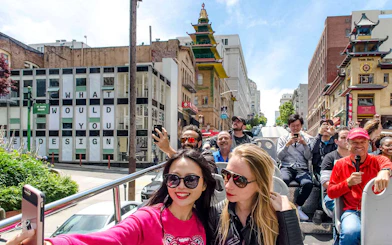 Open-top bus tour in San Francisco's Chinatown with tourists taking photos.