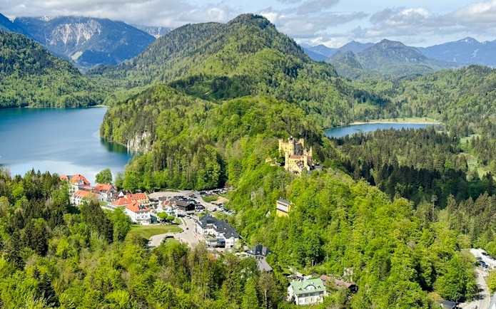 Hohenschwangau Castle surrounded by lush greenery and lakes in the Alps, Germany.