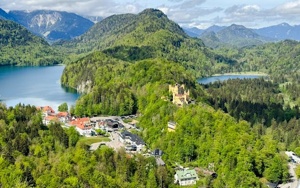 Hohenschwangau Castle surrounded by lush greenery and lakes in the Alps, Germany.