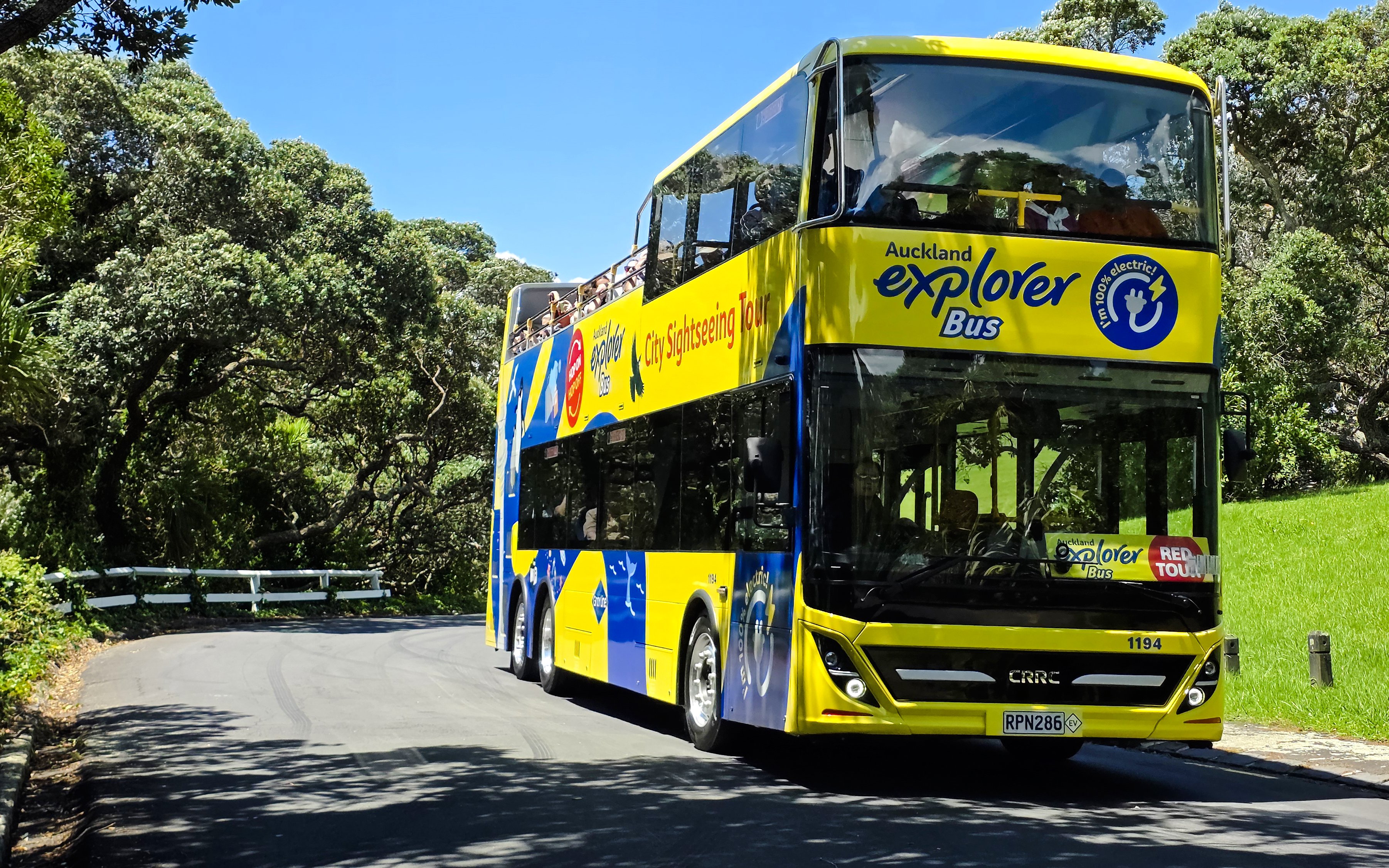 Auckland Explorer Bus on a scenic route through lush greenery.
