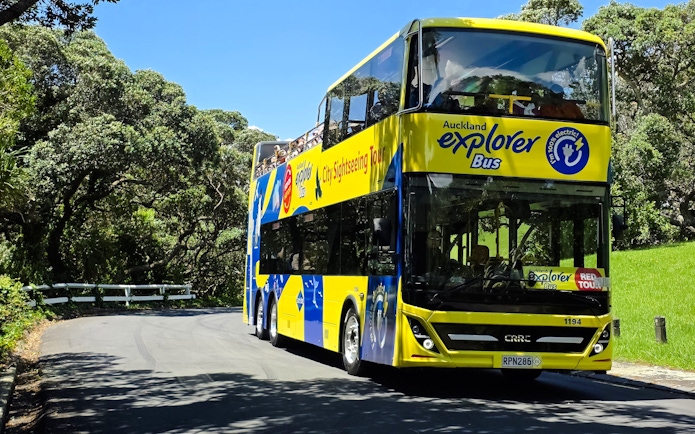 Auckland Explorer Bus on a scenic route through lush greenery.