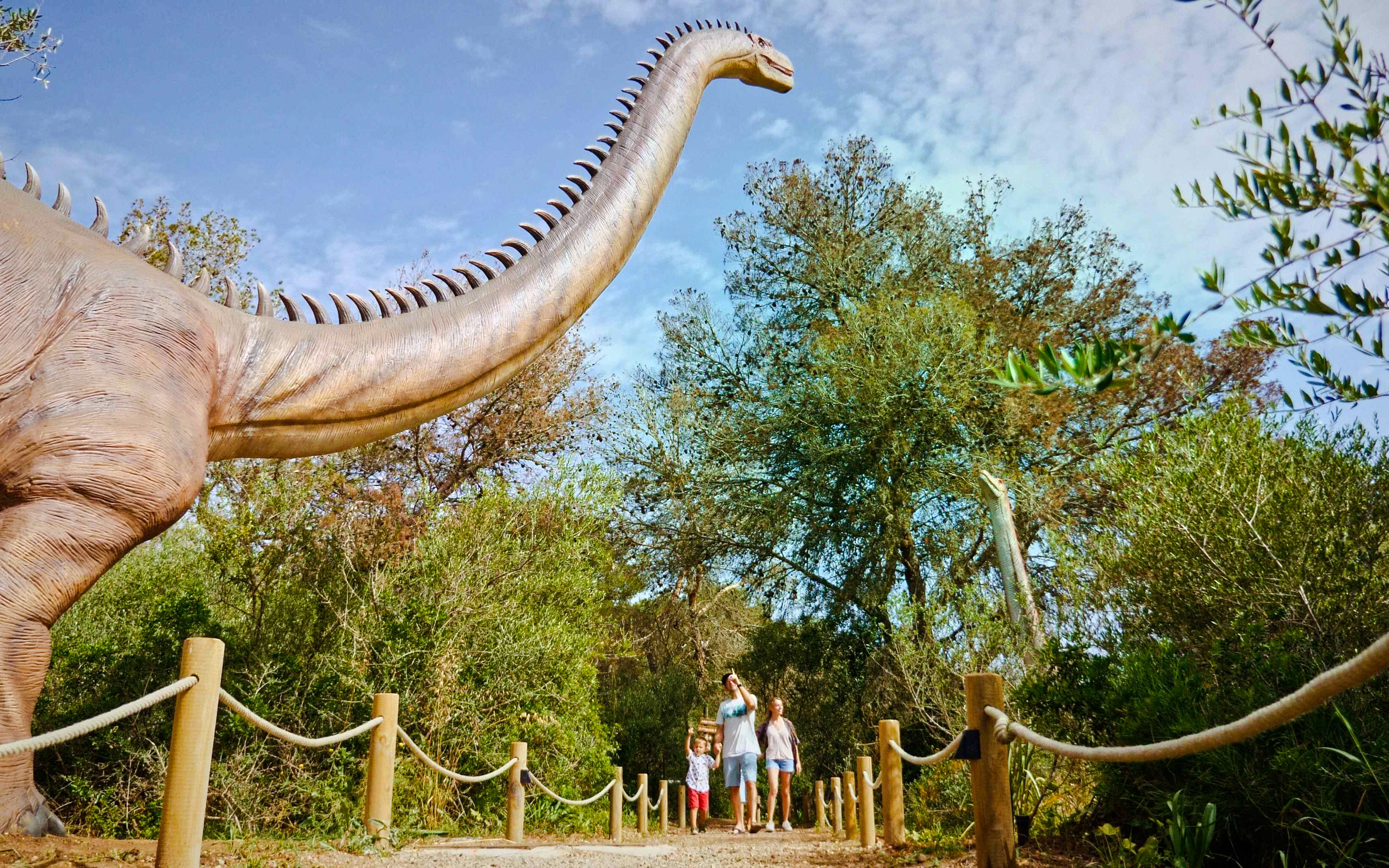 Visitors walking near a large dinosaur statue at Dinosaurland, Mallorca.