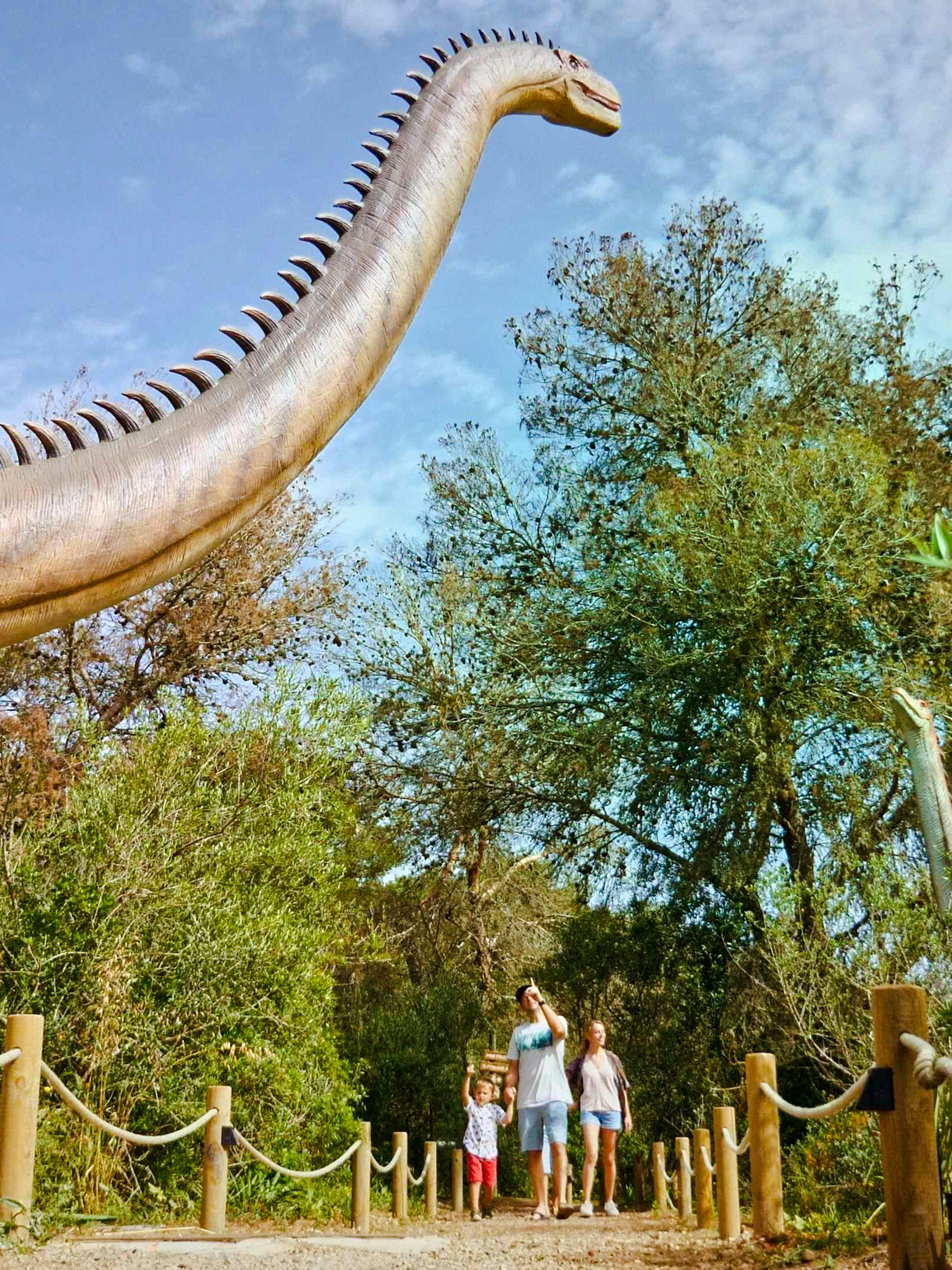 Visitors walking near a large dinosaur statue at Dinosaurland, Mallorca.