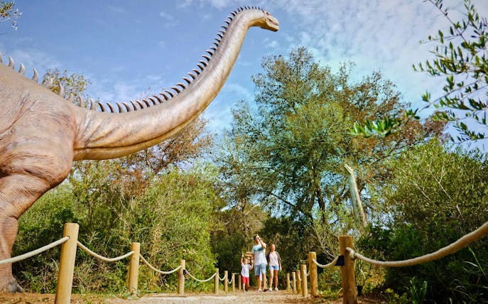 Visitors walking near a large dinosaur statue at Dinosaurland, Mallorca.