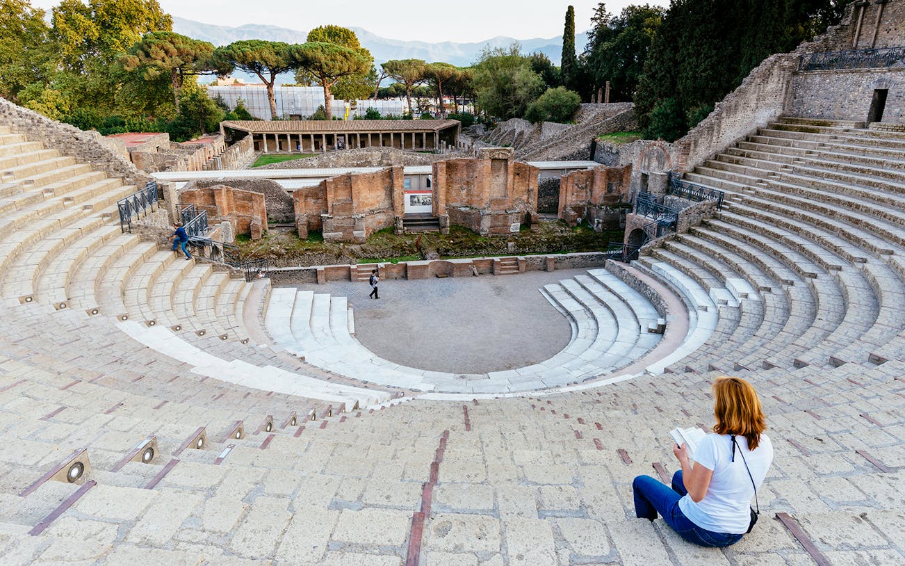 Woman reading a book in the ancient amphitheater of Pompeii, Italy.