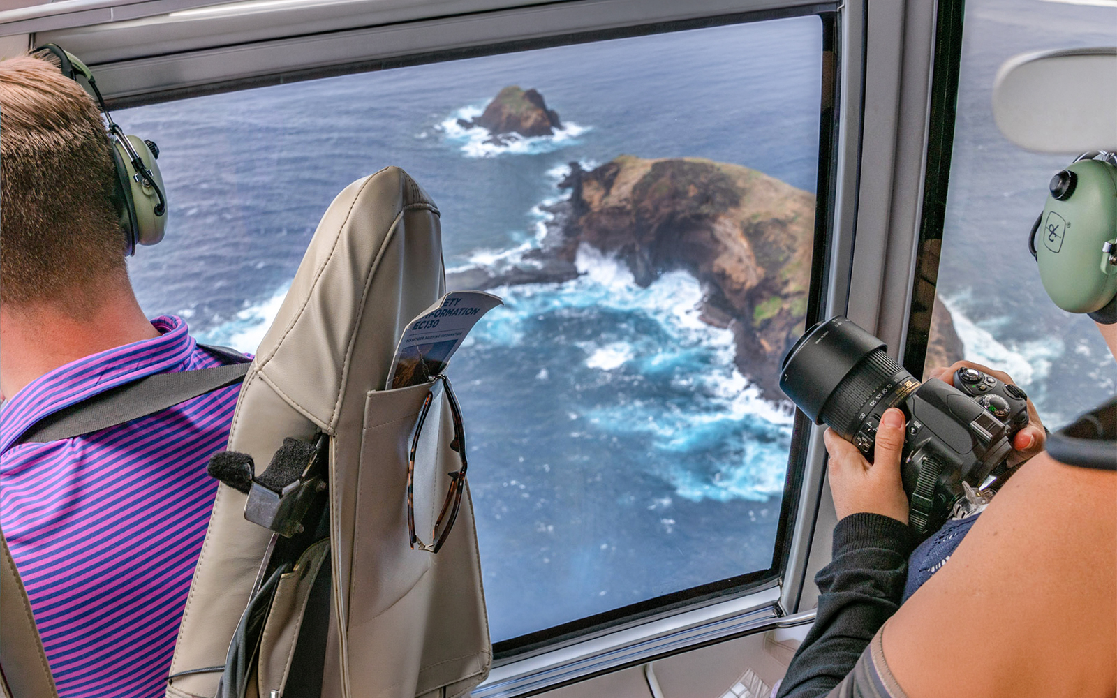 Helicopter view of Maui coastline with passengers photographing ocean cliffs.