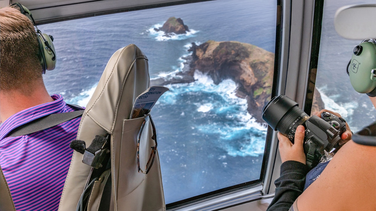 Helicopter view of Maui coastline with passengers photographing ocean cliffs.