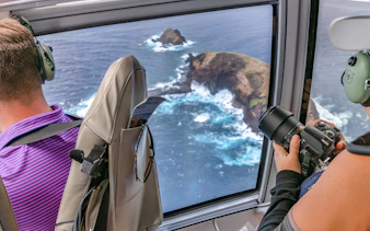 Helicopter view of Maui coastline with passengers photographing ocean cliffs.
