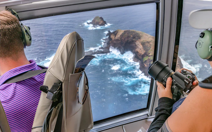Helicopter view of Maui coastline with passengers photographing ocean cliffs.