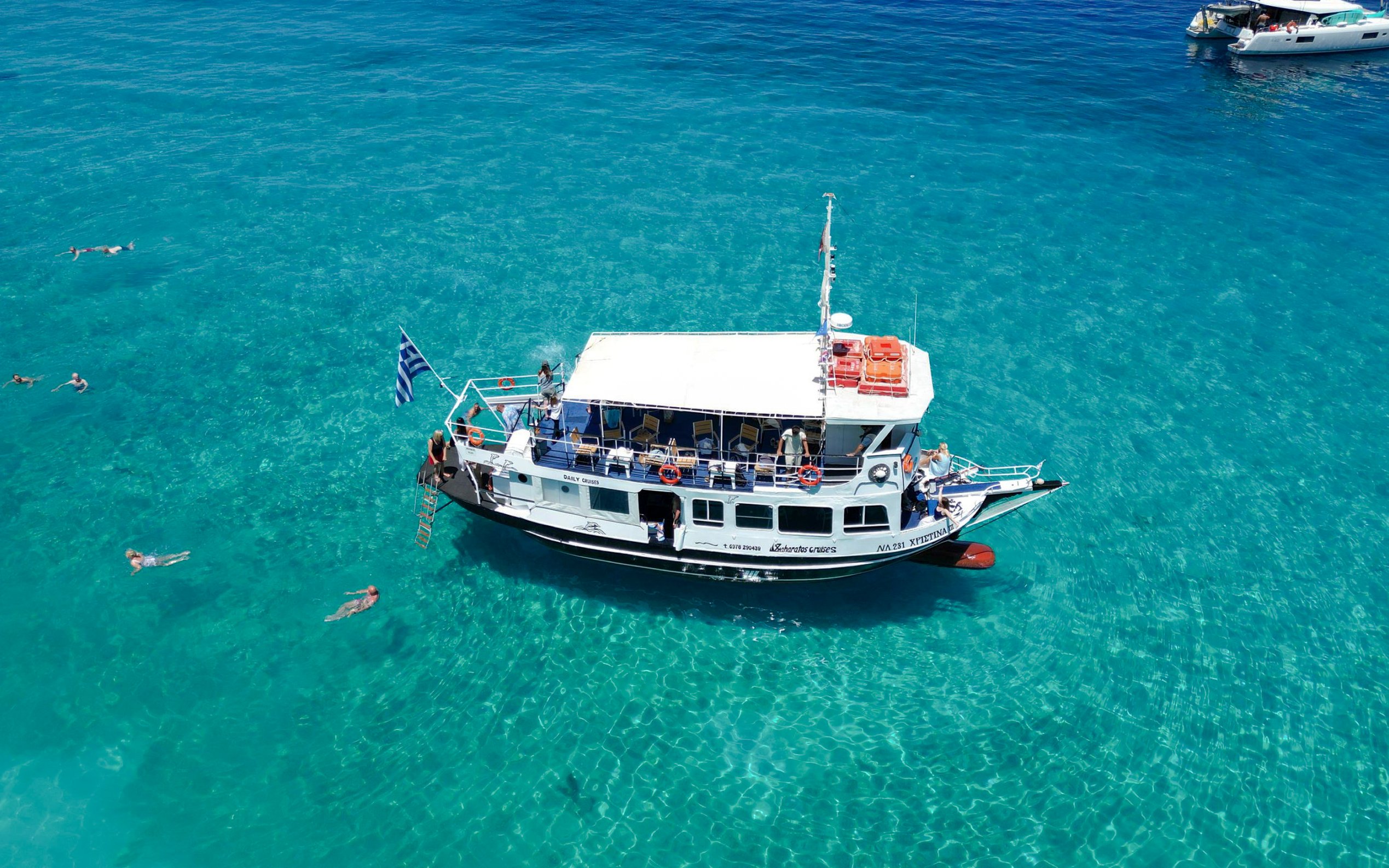 Cruise boat on clear blue waters with swimmers, Ithaca Cruise, Kefalonia, Greece.