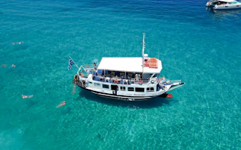 Cruise boat on clear blue waters with swimmers, Ithaca Cruise, Kefalonia, Greece.