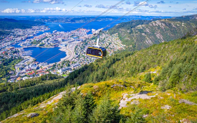 Ulriken cable car ascending over Bergen, Norway, with cityscape and fjord views.