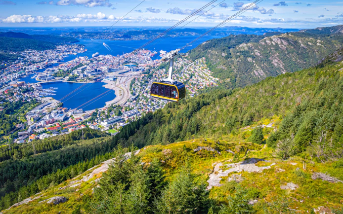 Ulriken cable car ascending over Bergen, Norway, with cityscape and fjord views.