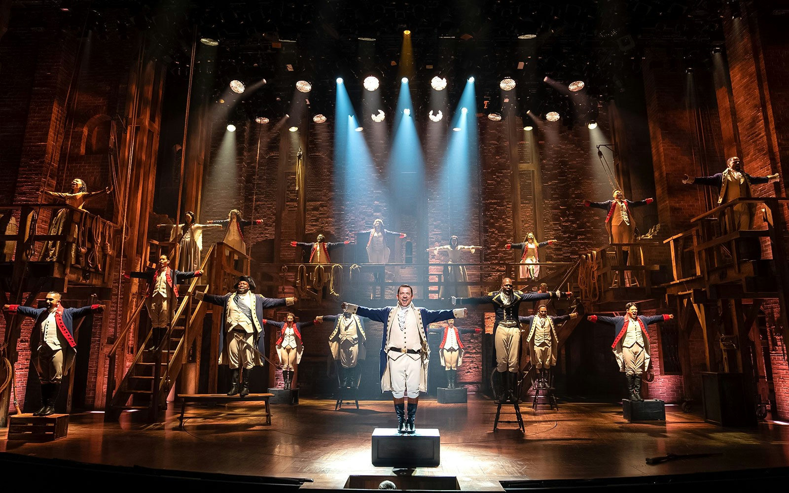 Stage performance of Hamilton cast in period costumes with dramatic lighting.