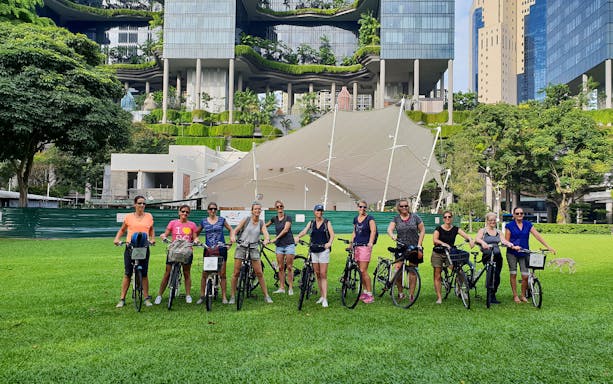 Group of cyclists on a guided historical bike tour in front of a modern building in Singapore.