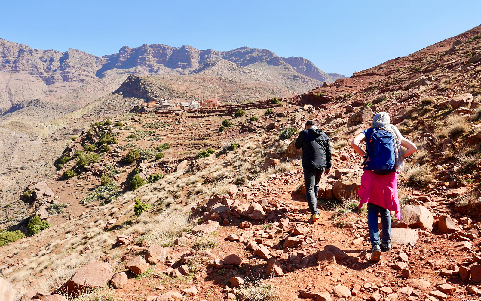 Hikers trekking rocky path in Ourika Valley towards traditional Berber village, Morocco.