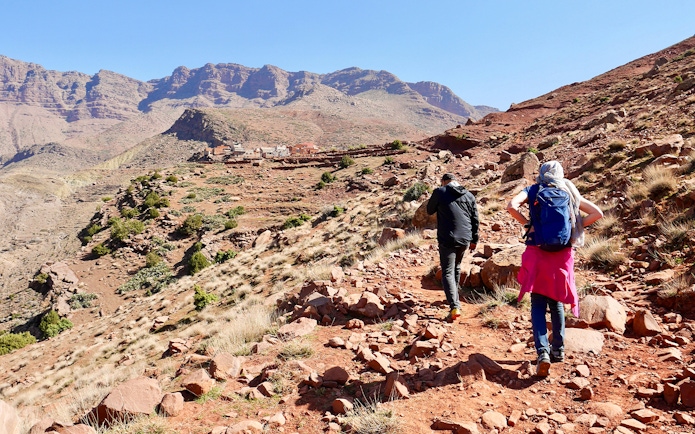 Hikers trekking rocky path in Ourika Valley towards traditional Berber village, Morocco.