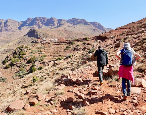 Hikers trekking rocky path in Ourika Valley towards traditional Berber village, Morocco.