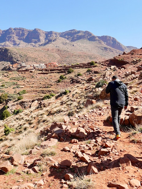 Hikers trekking rocky path in Ourika Valley towards traditional Berber village, Morocco.