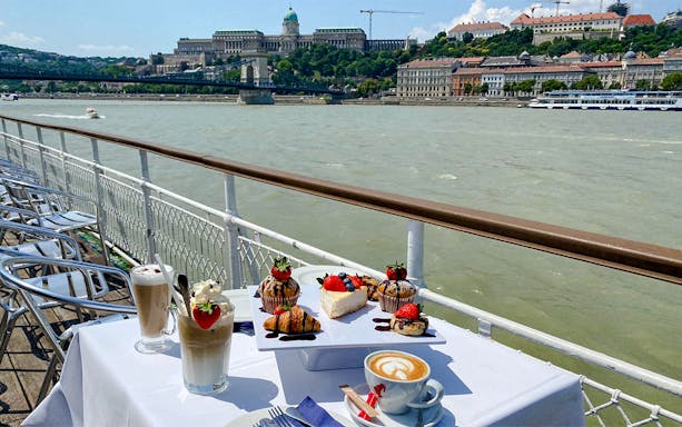 Guests enjoying summer brunch on Danube River cruise with Budapest Parliament building in the background.
