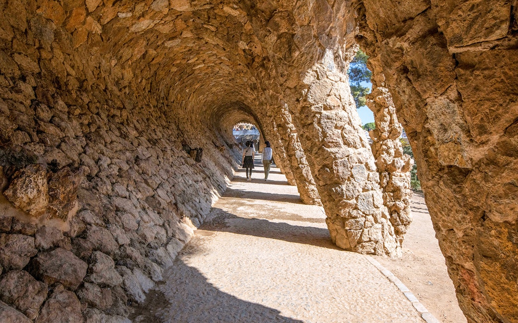 Visitors walking through stone arches in Park Güell, Barcelona.