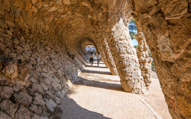 Visitors walking through stone arches in Park Güell, Barcelona.