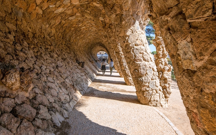 Visitors walking through stone arches in Park Güell, Barcelona.