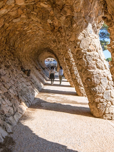 Visitors walking through stone arches in Park Güell, Barcelona.