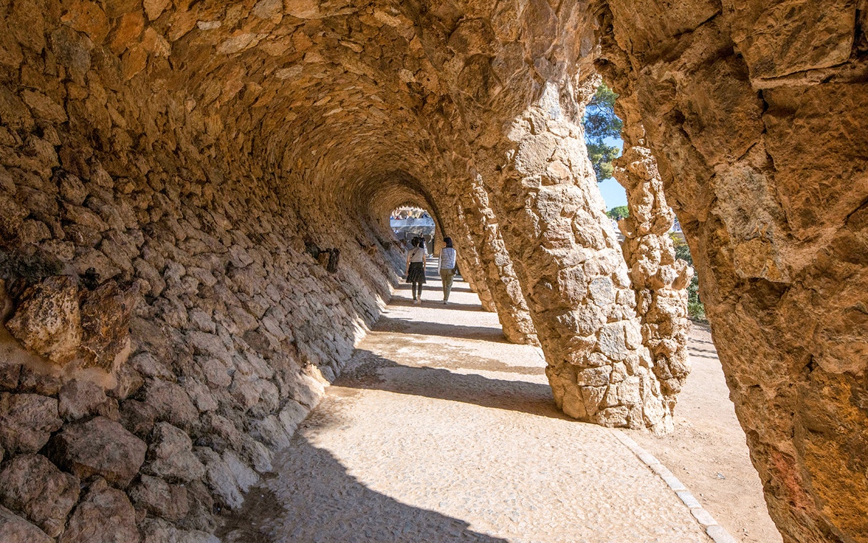 Visitors walking through stone arches in Park Güell, Barcelona.