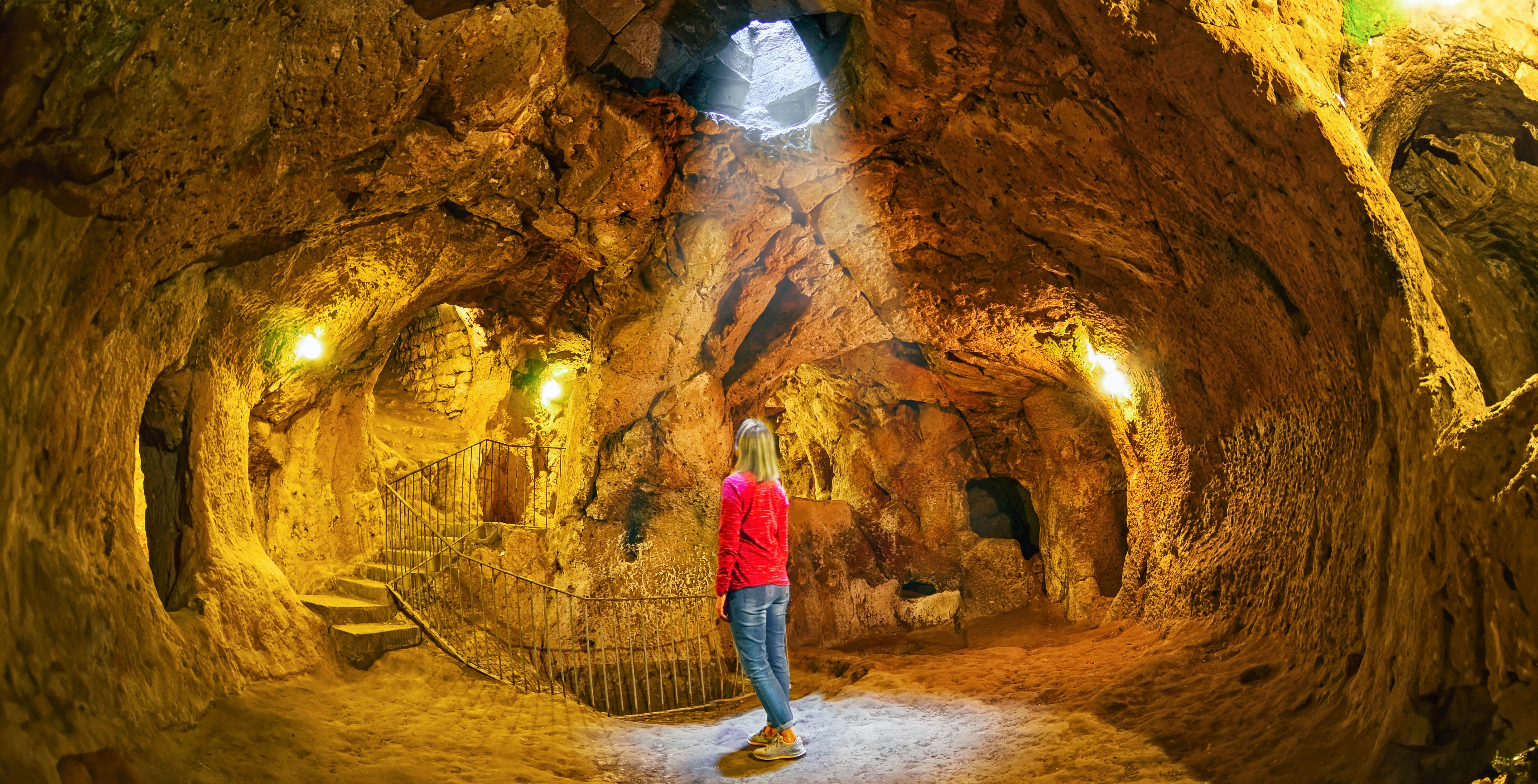 Visitor exploring Ozkonak Underground City cave with stone walls and natural light.