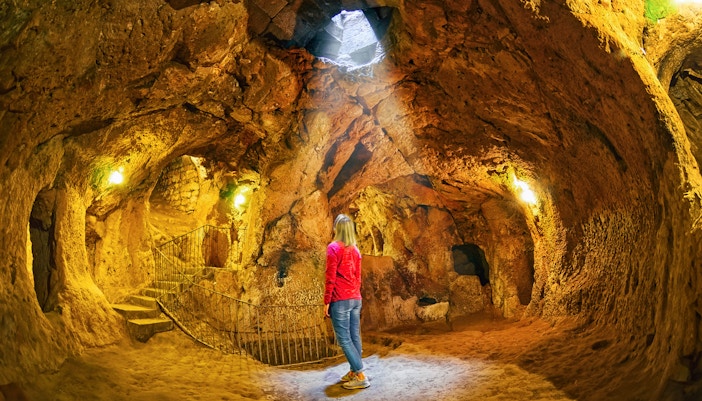 Visitor exploring Ozkonak Underground City cave with stone walls and natural light.