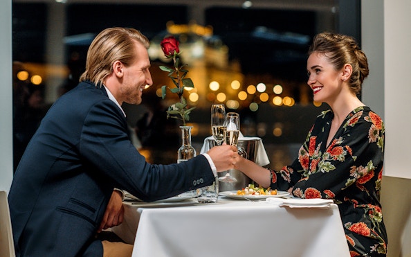 Couple enjoying a romantic dinner cruise in Prague with city lights in the background.