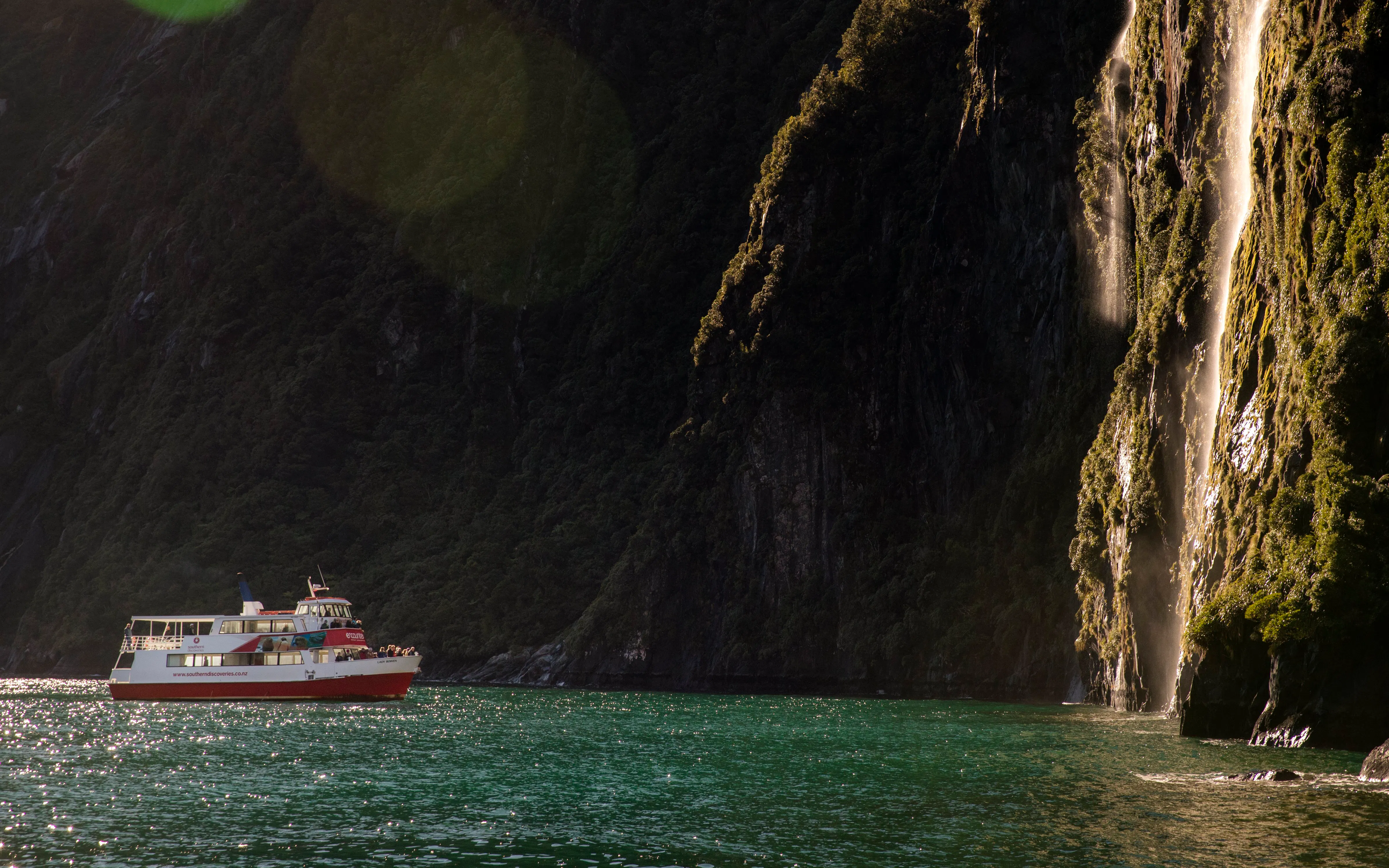 Cruise boat near waterfall in Milford Sound, New Zealand.