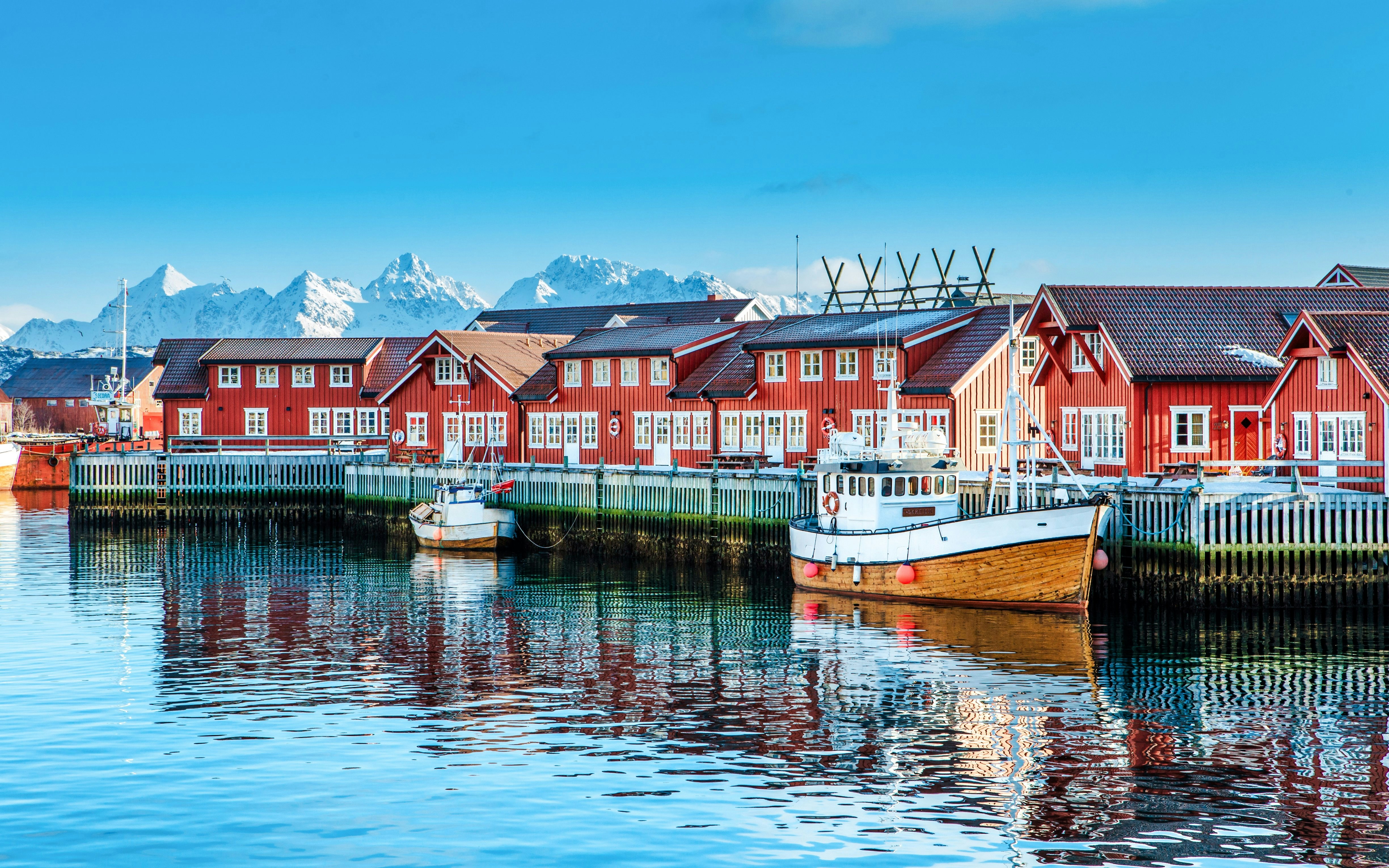 Red wooden buildings and boats at Svolvaer harbor, Lofoten with snowy mountains in the background.