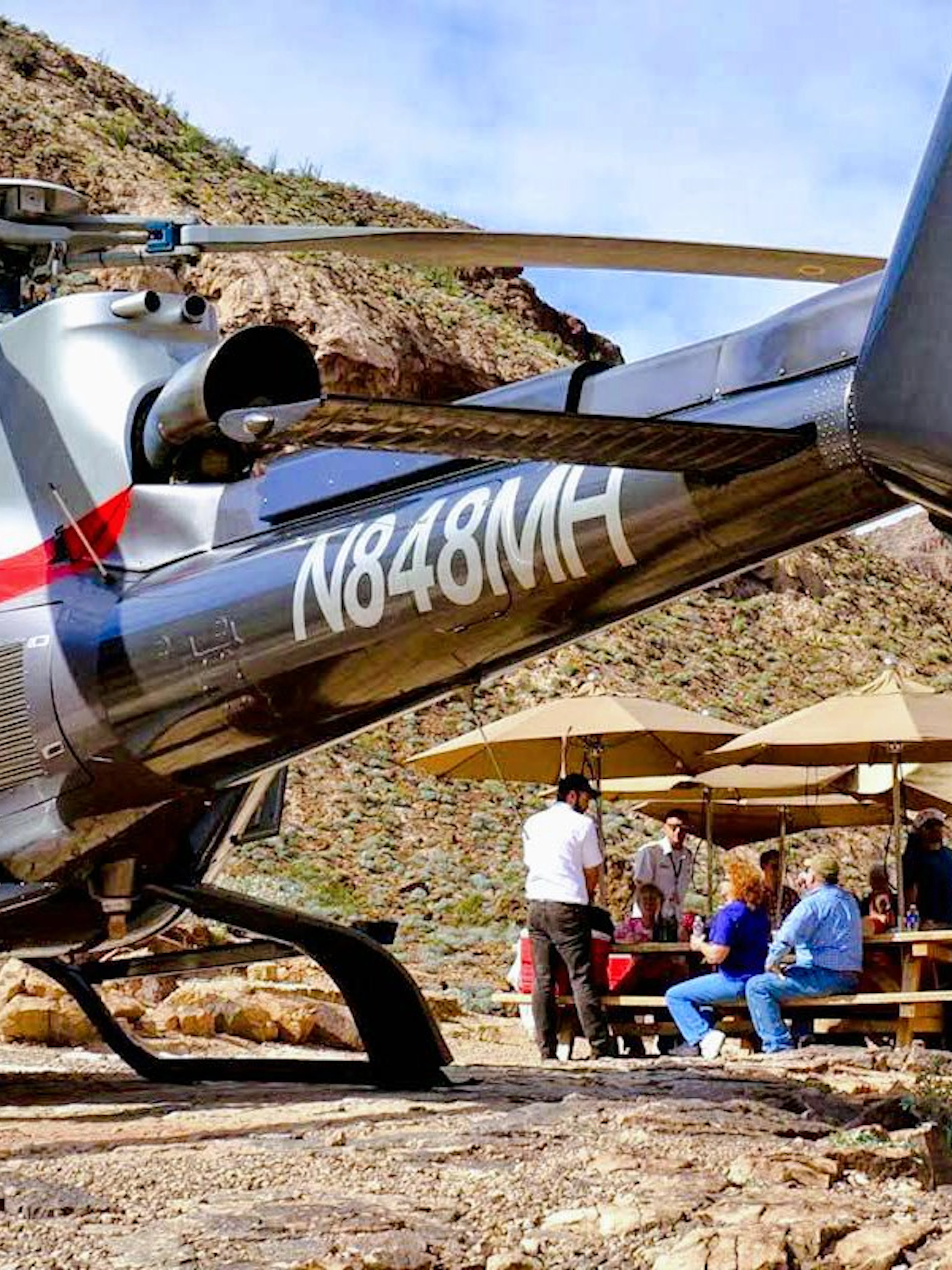 Helicopter landed at Grand Canyon West with tourists enjoying a picnic under umbrellas.