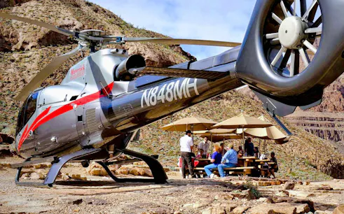 Helicopter landed at Grand Canyon West with tourists enjoying a picnic under umbrellas.