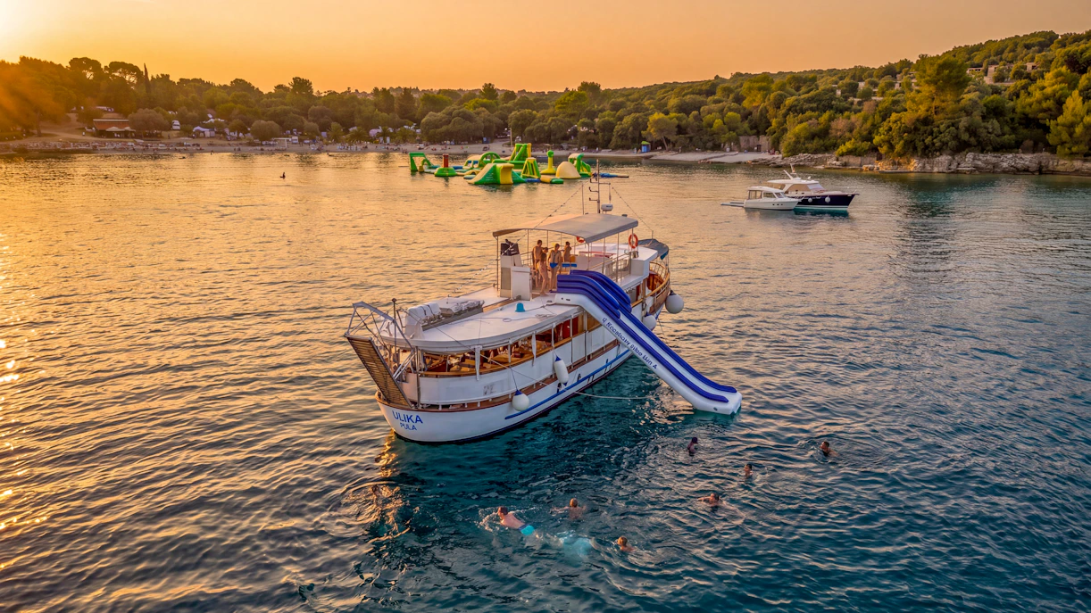 Boat with slide on Brijuni National Park tour at sunset, Pula, with swimmers in the sea.