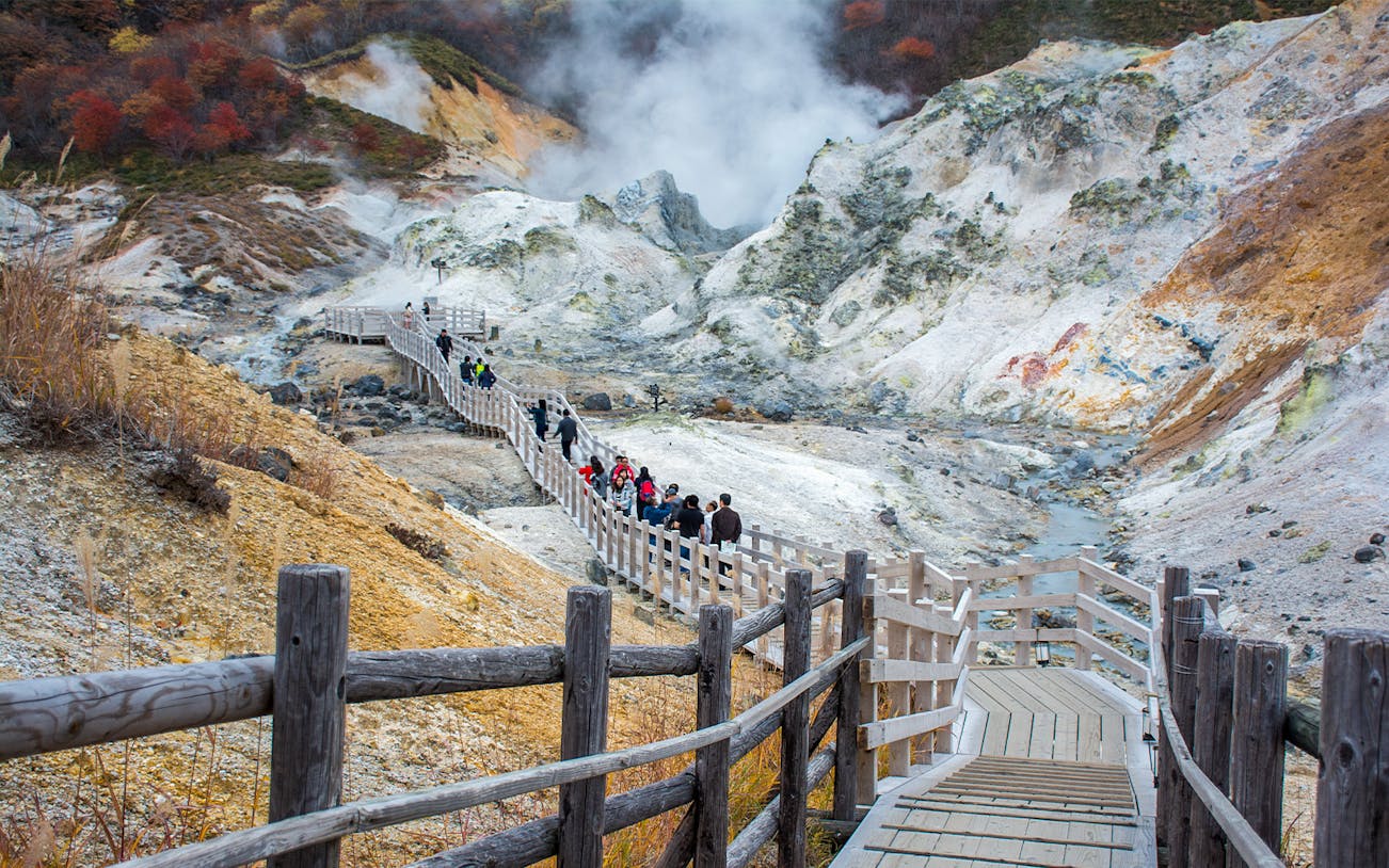 Visitors walking on a wooden path through Jigokudani's volcanic landscape in Hokkaido.