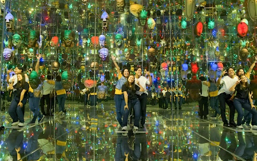 Group posing in mirrored room with colorful masks at Asana Artseum, Garuda Wisnu Kencana, Bali.