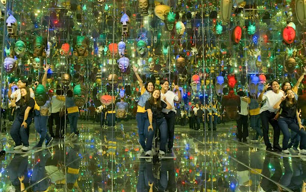 Group posing in mirrored room with colorful masks at Asana Artseum, Garuda Wisnu Kencana, Bali.
